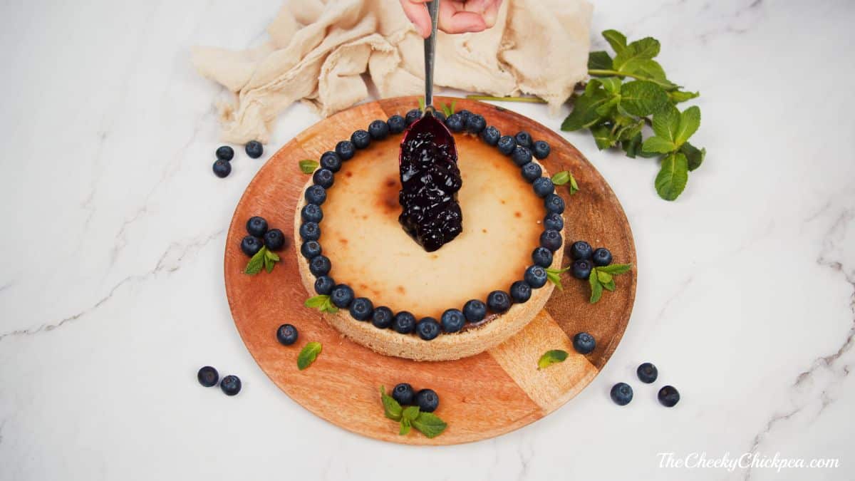blueberry sauce being spooned on top of cheesecake