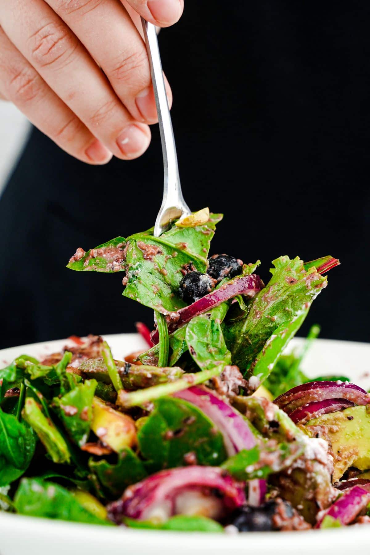 forkfull of salad held above white bowl with black background