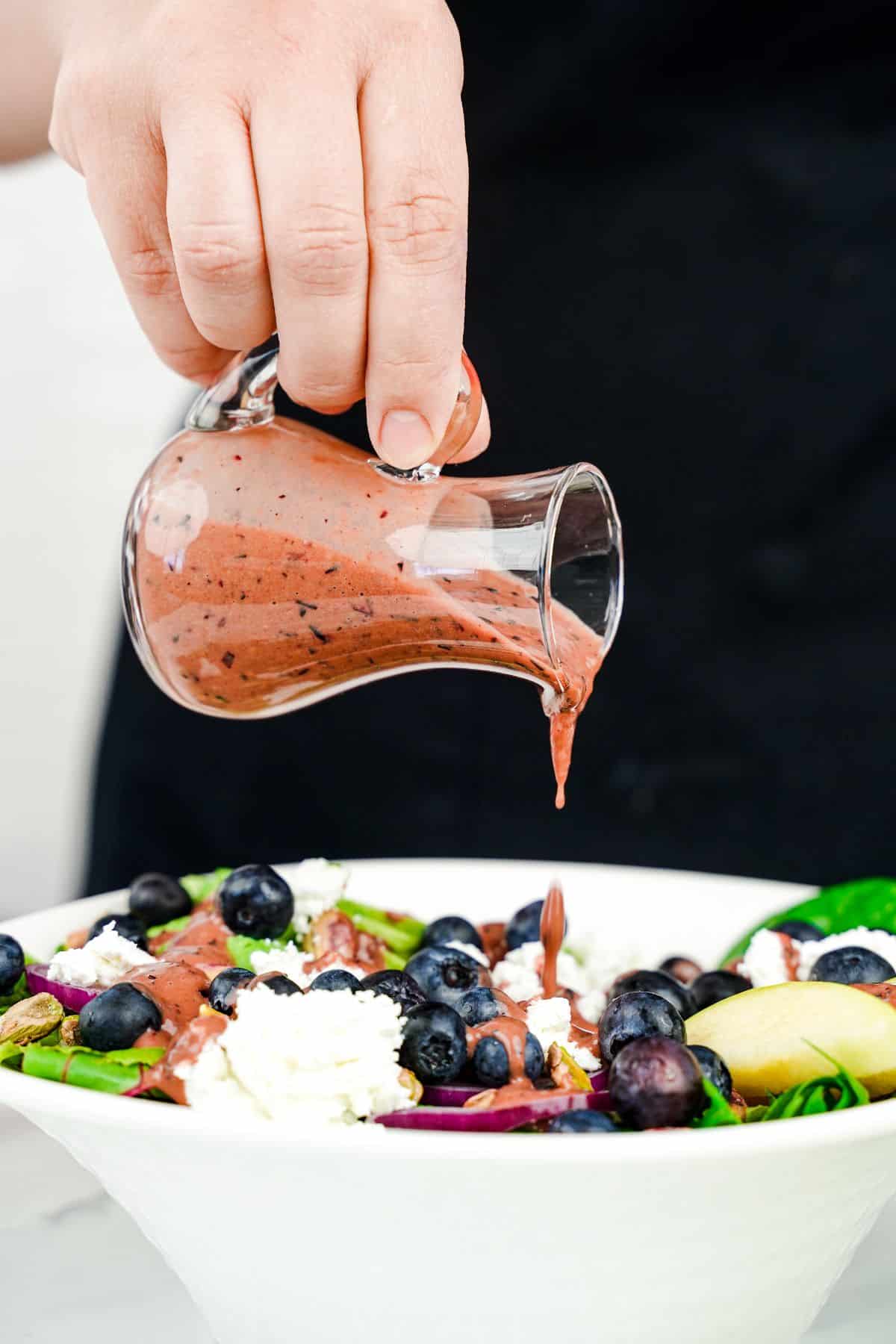 jar of salad dressing being poured over salad in white bowl