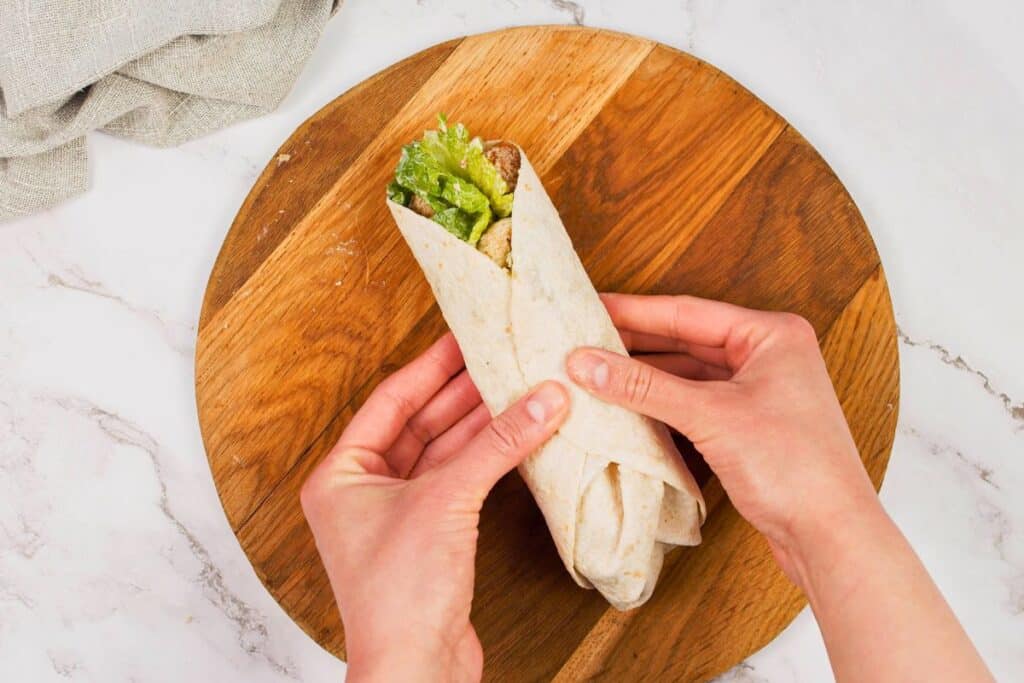 hand holding vegan Caesar wrap above round wood platter