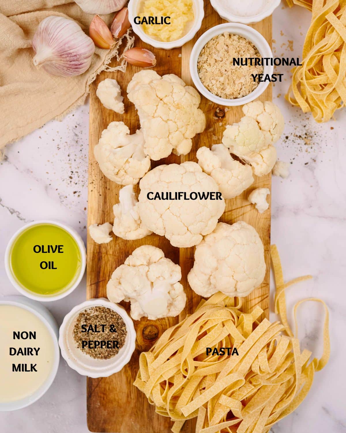 ingredients for cauliflower alfredo on wooden cutting board on marble table