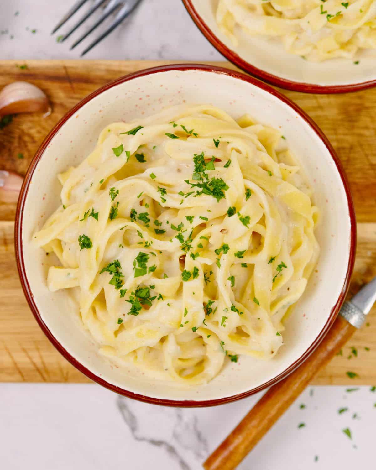 wooden board on white marble table holding bowl of pasta with vegan cauliflower alfredo on top