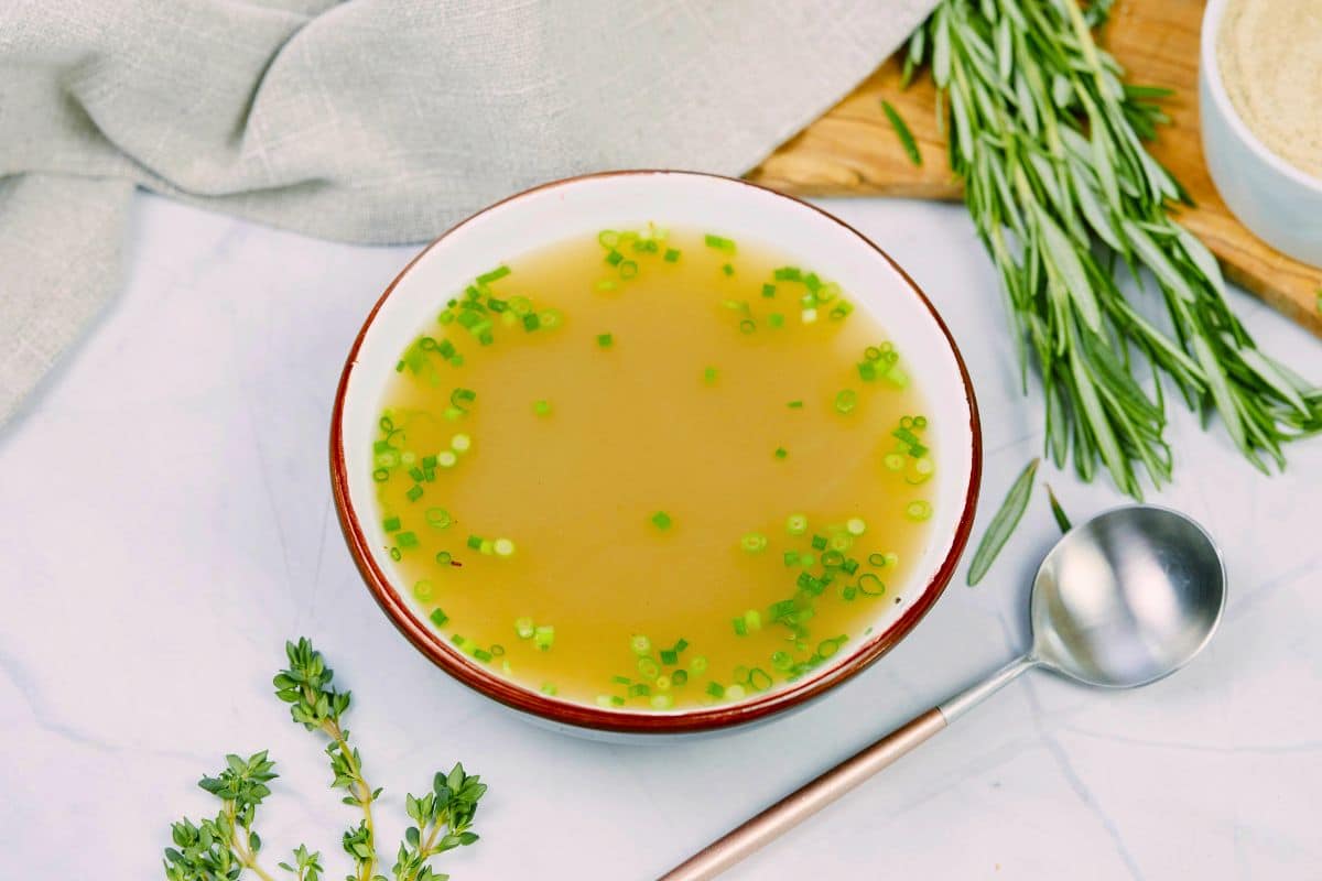 white bowl of broth with green onions on top