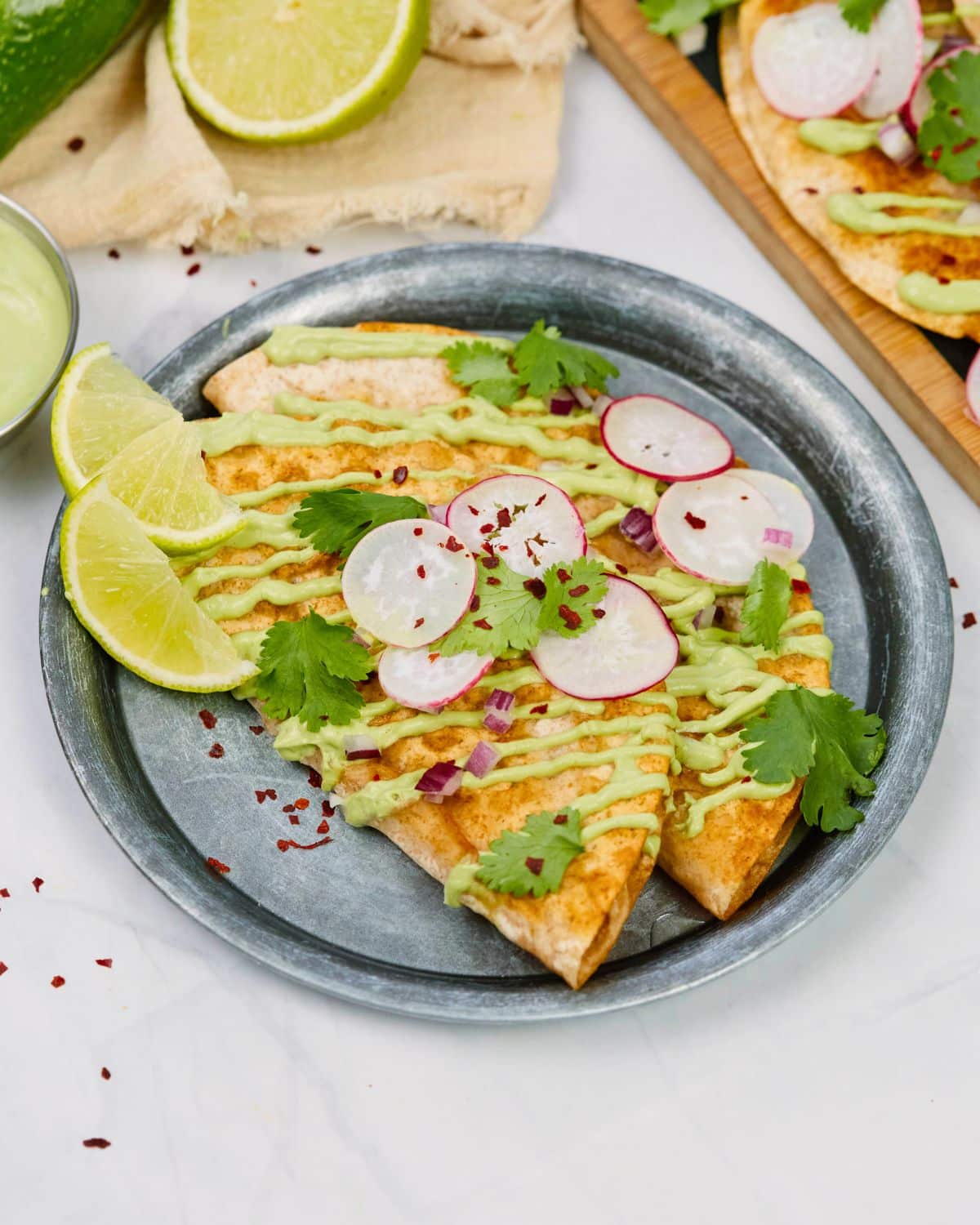 gray plate holding tacos with sliced radishes and lime wedges on top