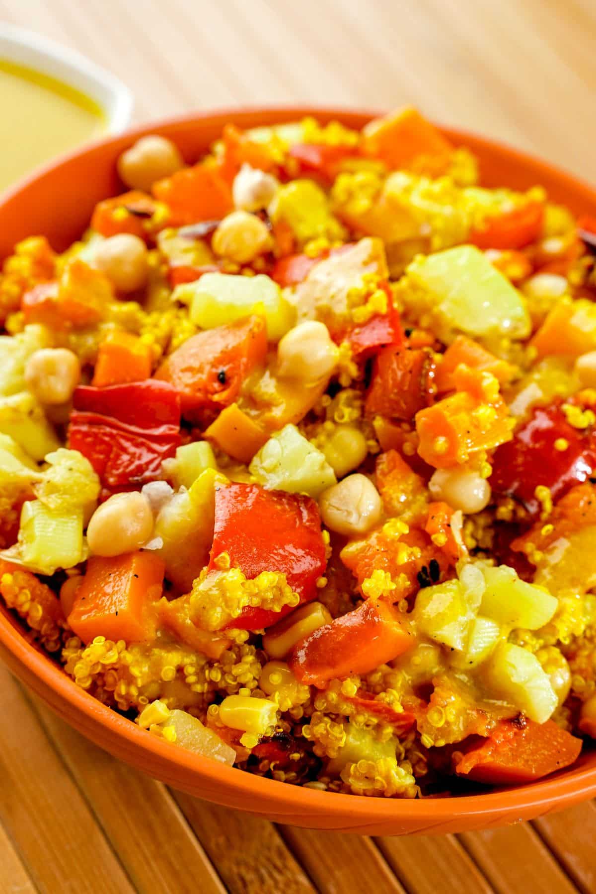 orange bowl of quinoa salad with chickpeas and squash on top of wood table