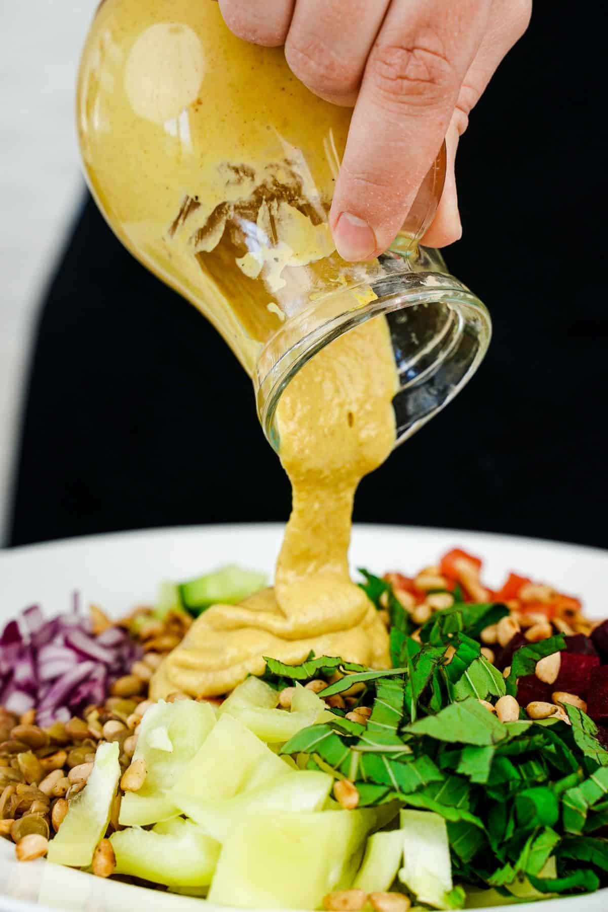 salad dressing being poured over lentil chickpea salad in white bowl