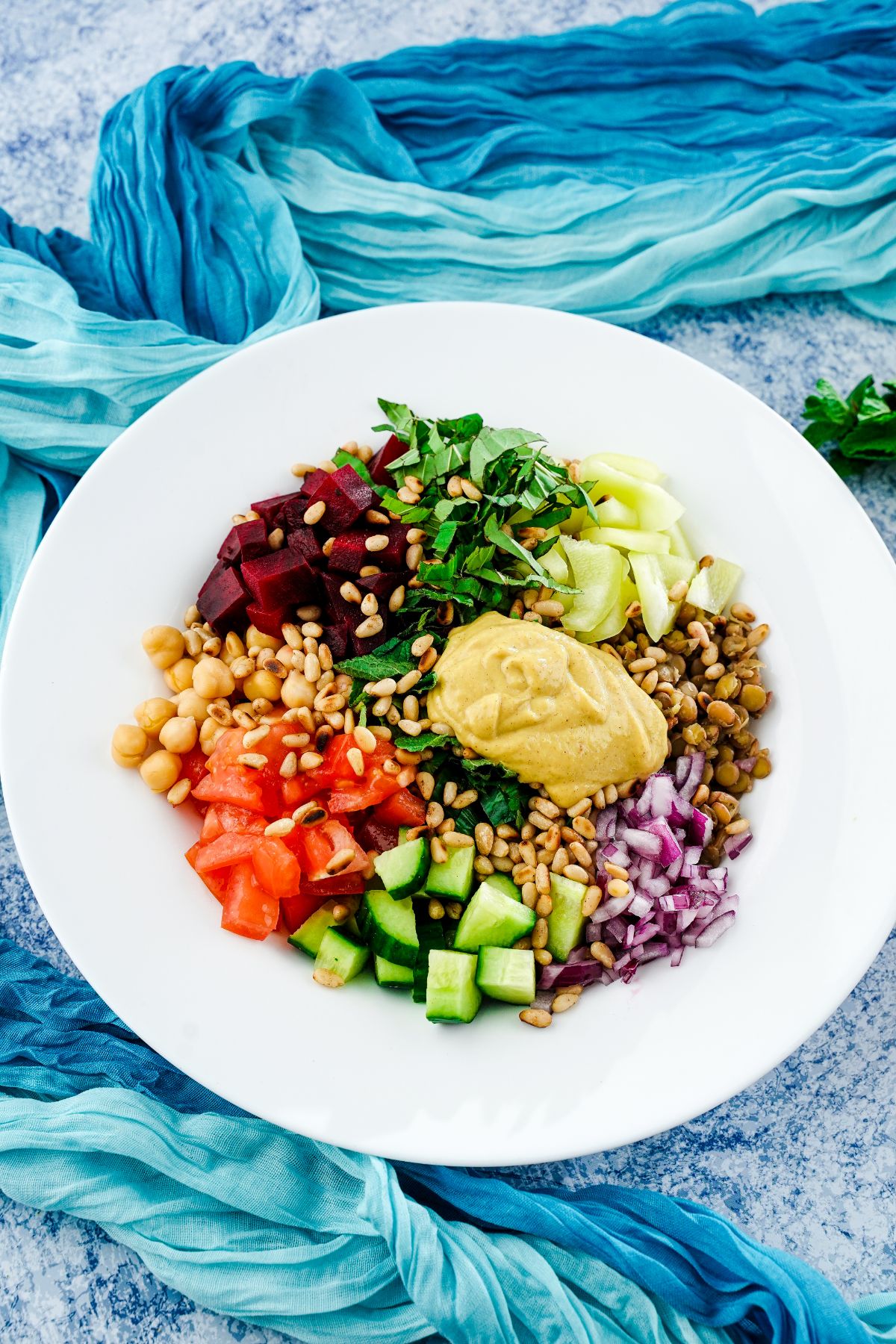 white bowl with colorful vegetables and lentils on top of teal cloth tablecloth