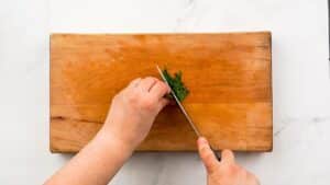 herbs being chopped on wood cutting board