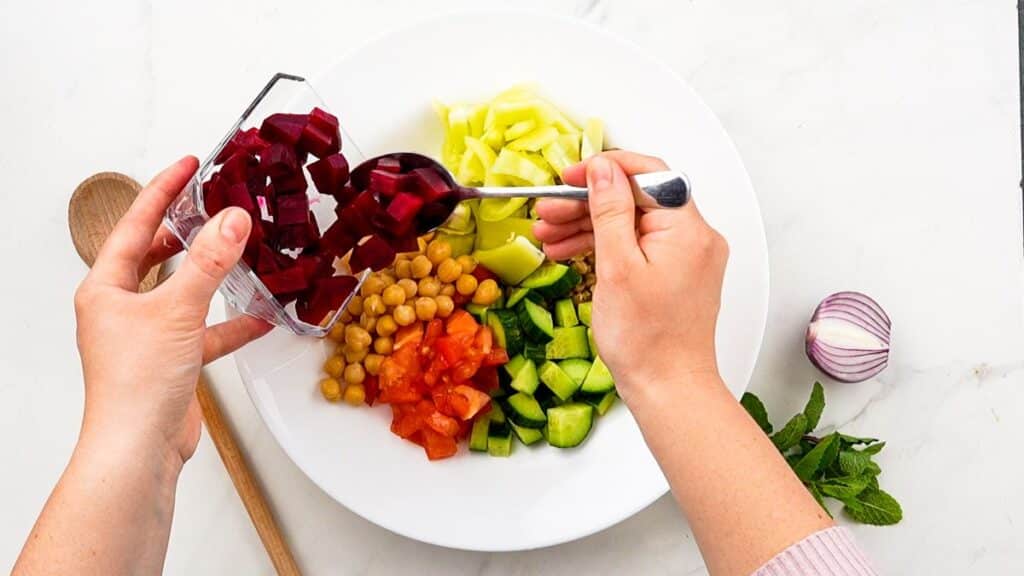 beets being poured on top of white bowl of salad