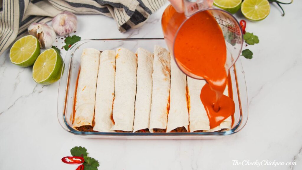 enchiladas in baking dish with sauce being poured over the top