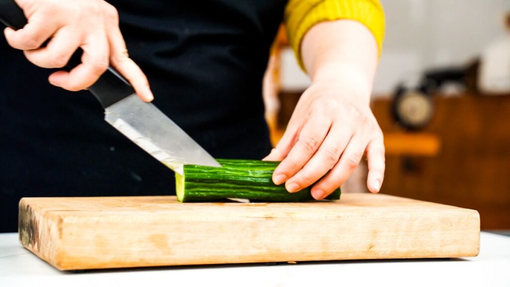 hand using knife to slice cucumber on cutting board