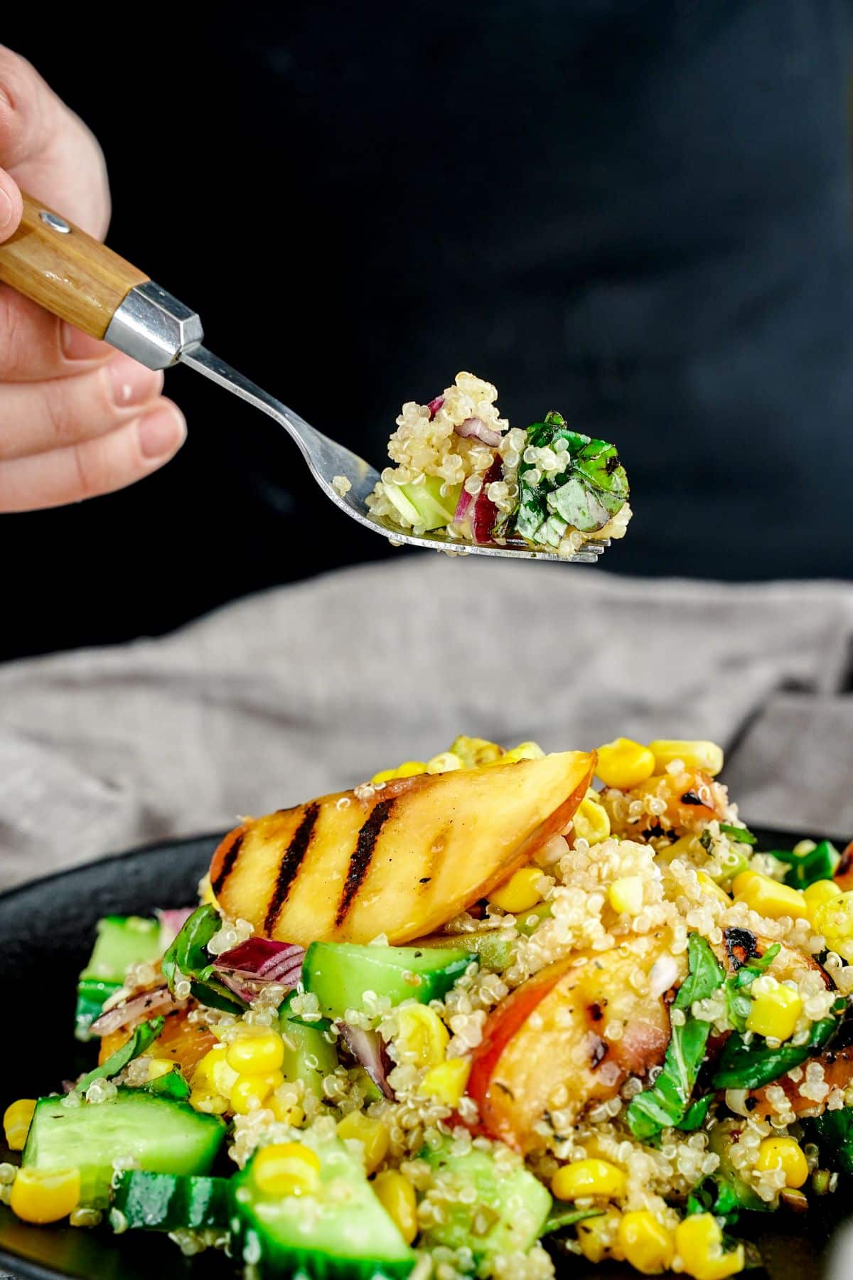 spoon of salad held above black plate of grilled peach quinoa salad