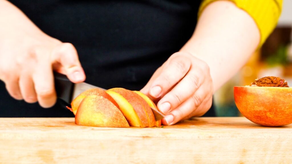 hand slicing a peach on wooden cutting board