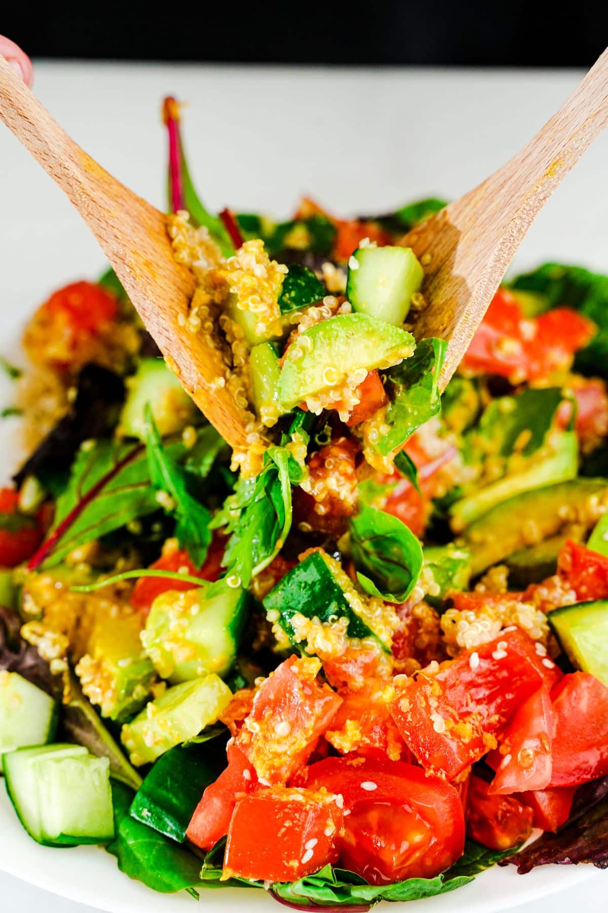 wooden spoon and fork tossing salad above bowl