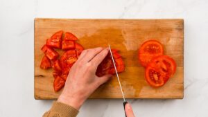 tomato being cubed on cutting board