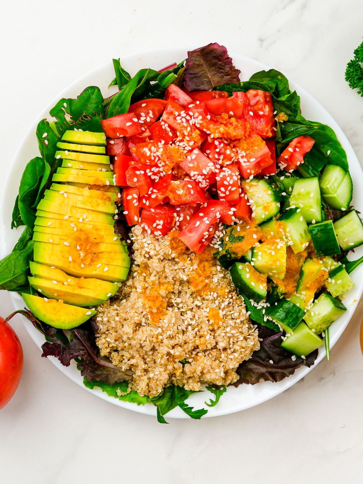 white bowl of mixed greens topped by sliced avocado, quinoa, tomatoes, and cucumbers