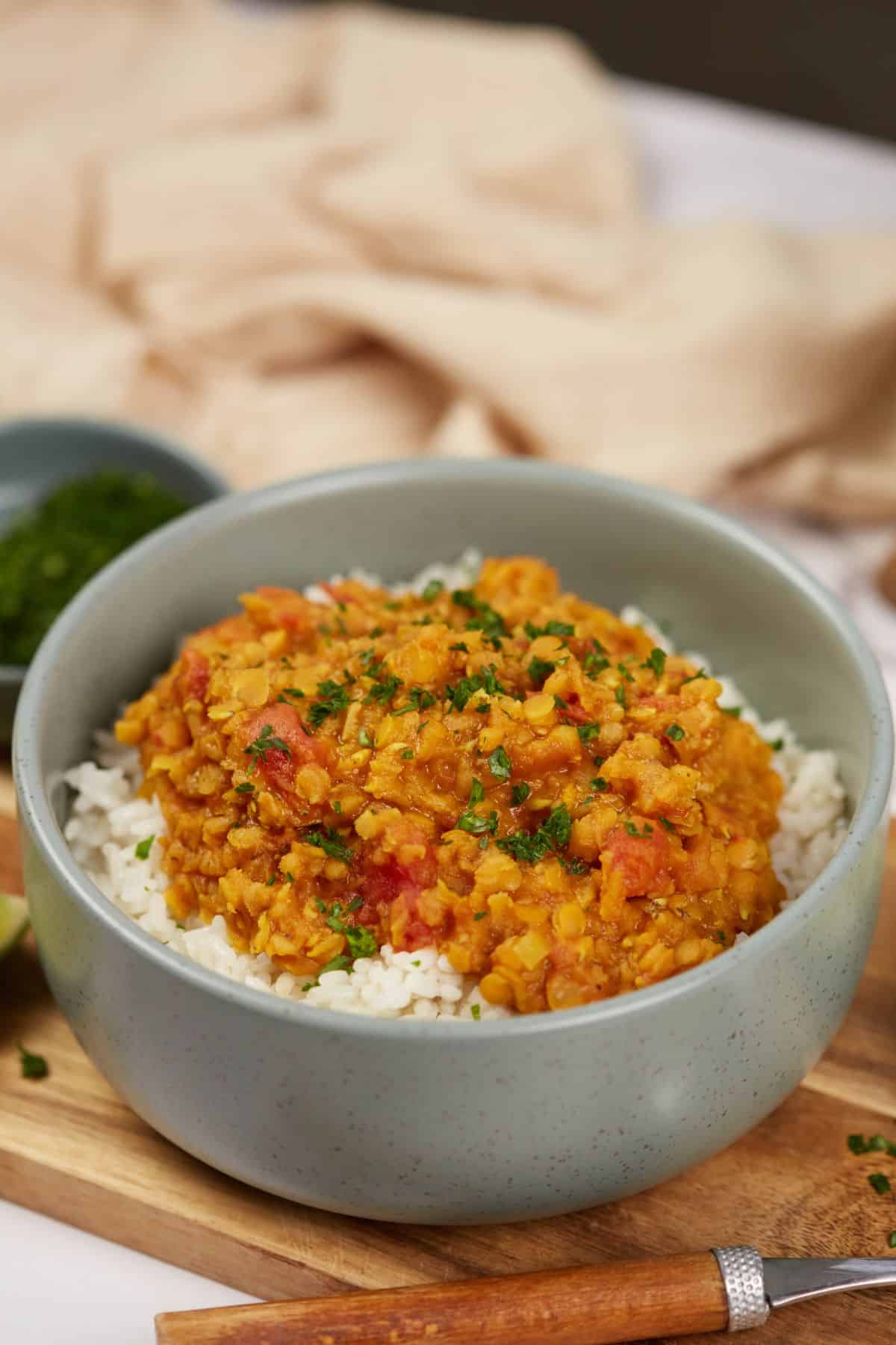 lentil dahl in bowl with rice on wood board by cream napkin