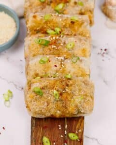 fresh green onions and sesame seeds on top of spring rolls on serving board