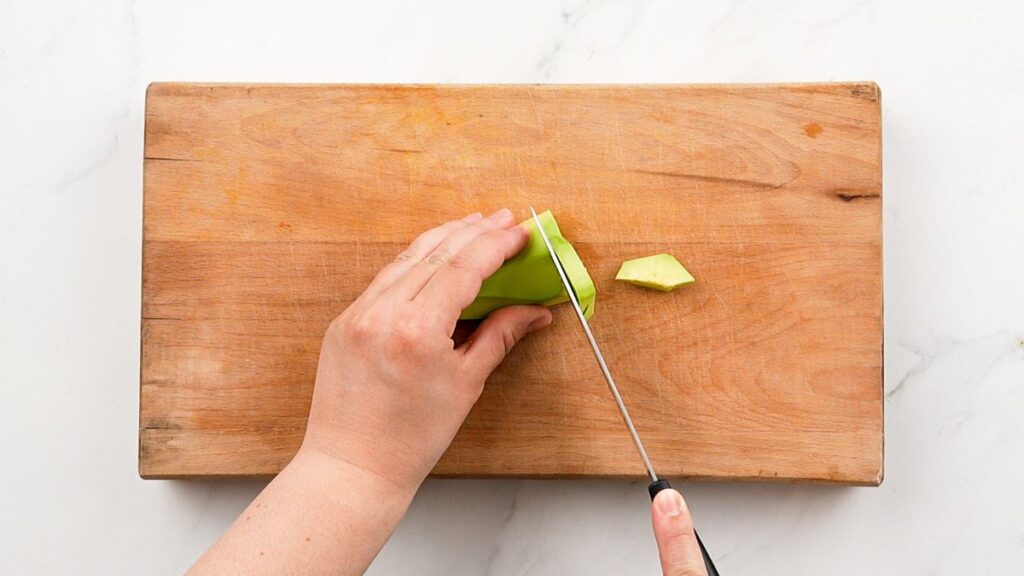 avocado being sliced on wooden cutting board