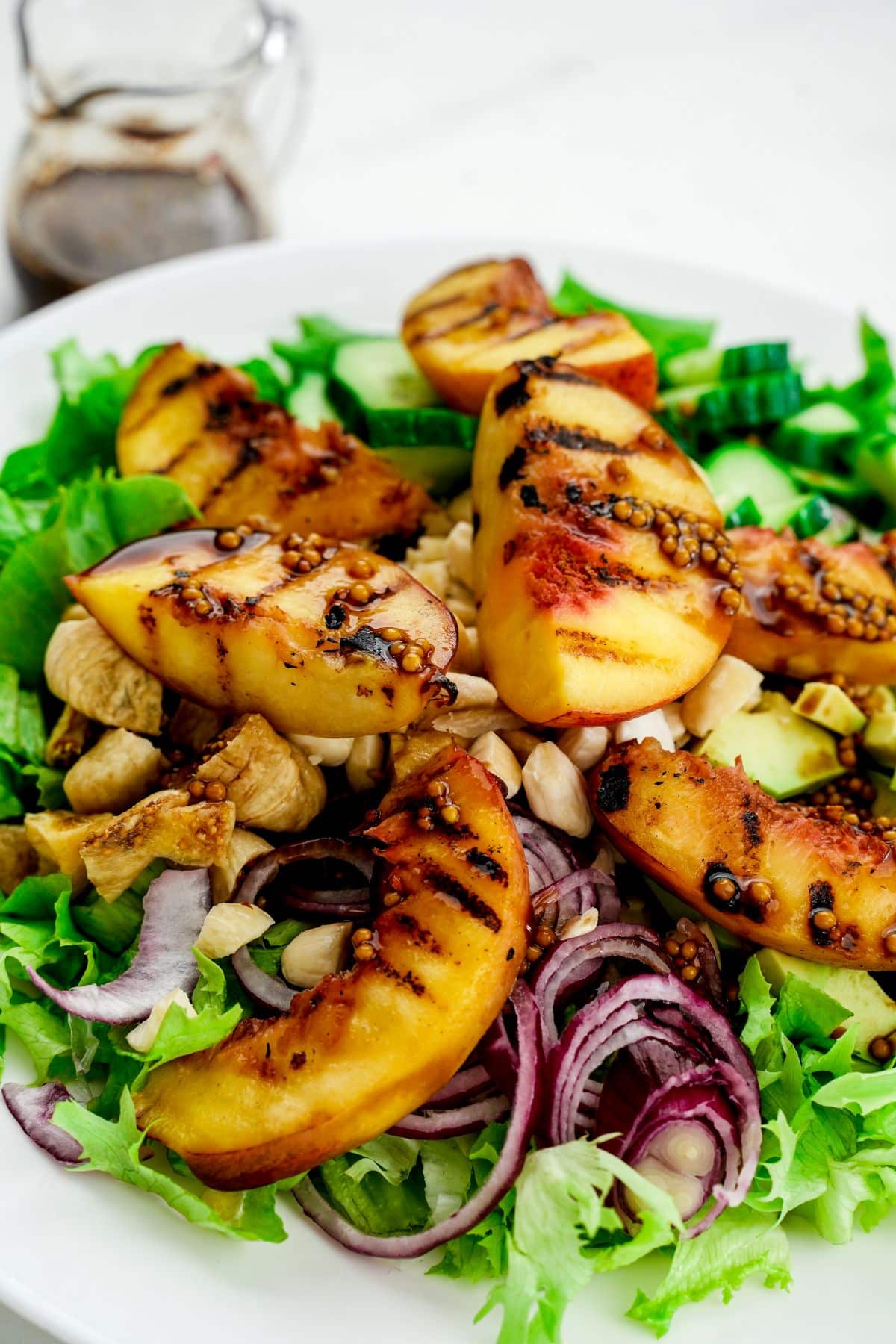 white bowl of salad topped by red onions and peaches