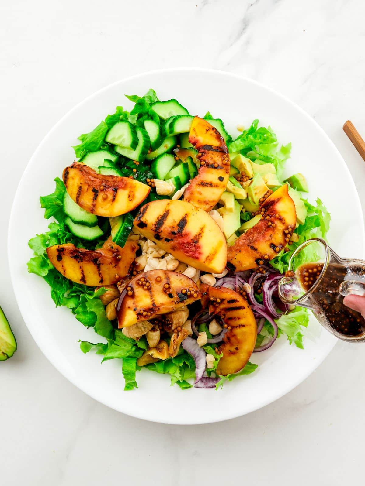 dressing biing poured over white plate of savory summer salad with peaches on top