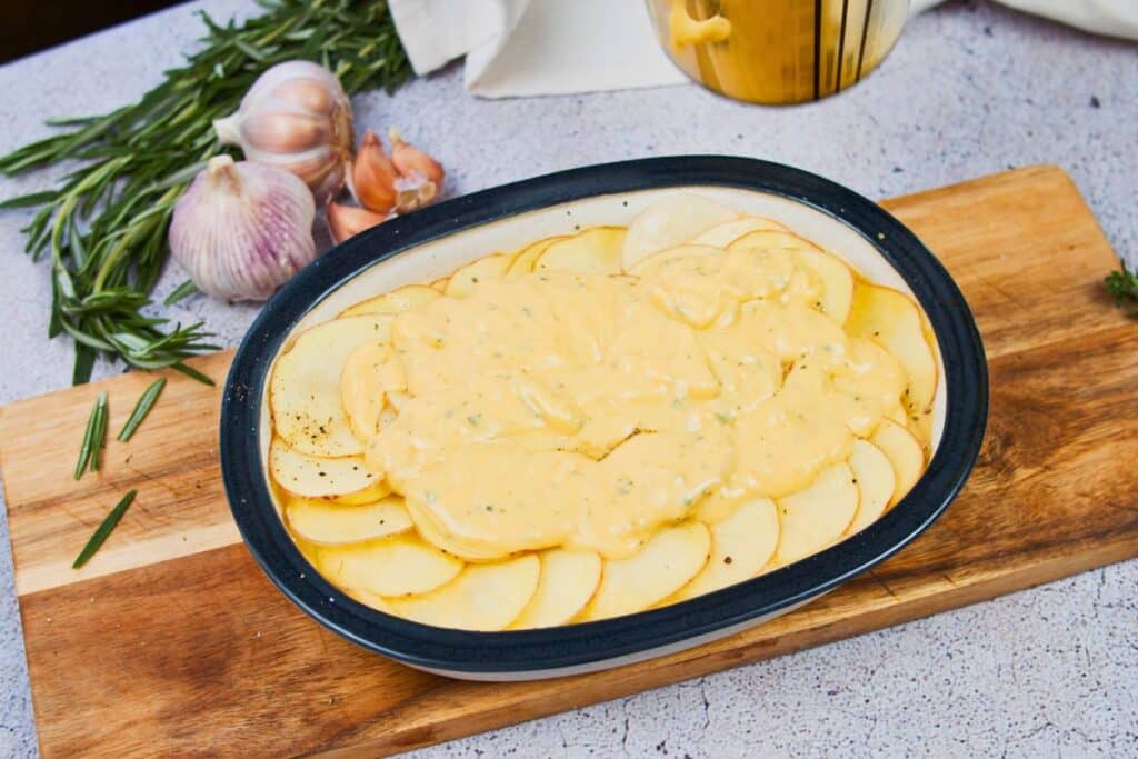 cheese sauce on top of sliced potatoes in baking dish