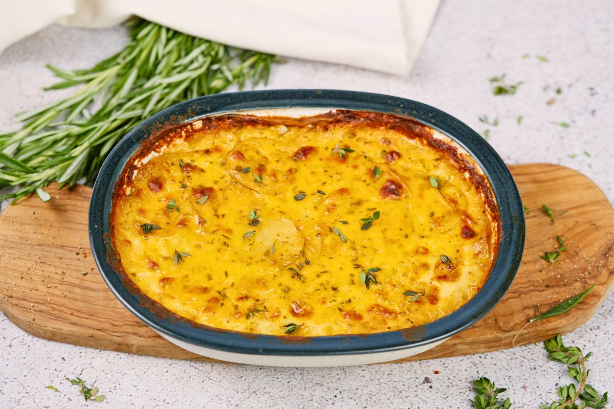 blue oval baking dish filled with potatoes on wooden board by fresh herbs