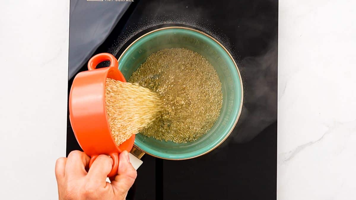 quinoa being poured into teal saucepan on black hotplate