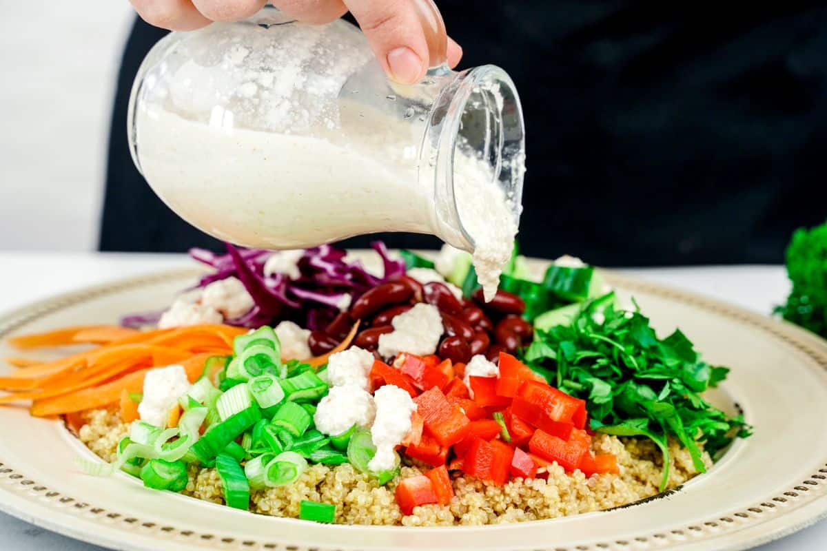 dressing being poured over rainbow salad on cream and gold plate