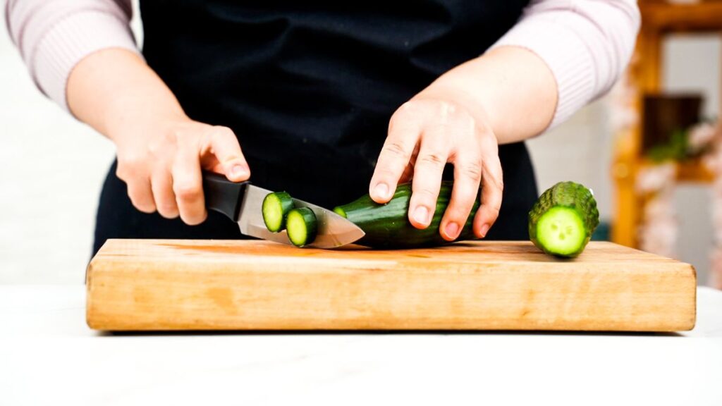 cucumber being sliced on cutting board
