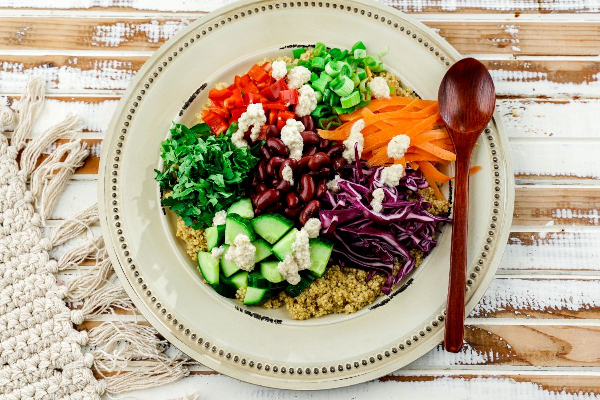 cream plate on wood table with rainbow sesame quinoa salad on plate by wooden spoon