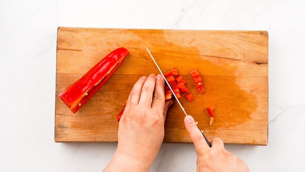 red bell pepper being chopped on cutting board