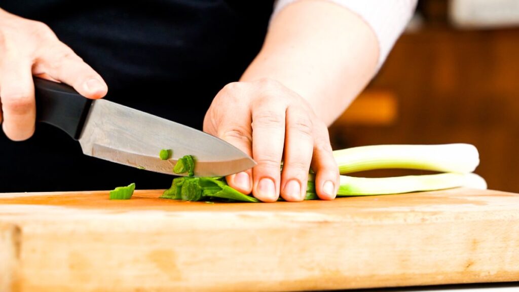 green onion being chopped on a wooden cutting board