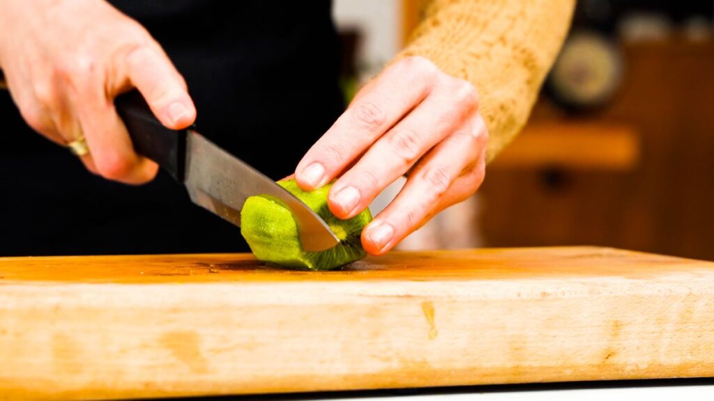 kiwi being sliced on cutting board