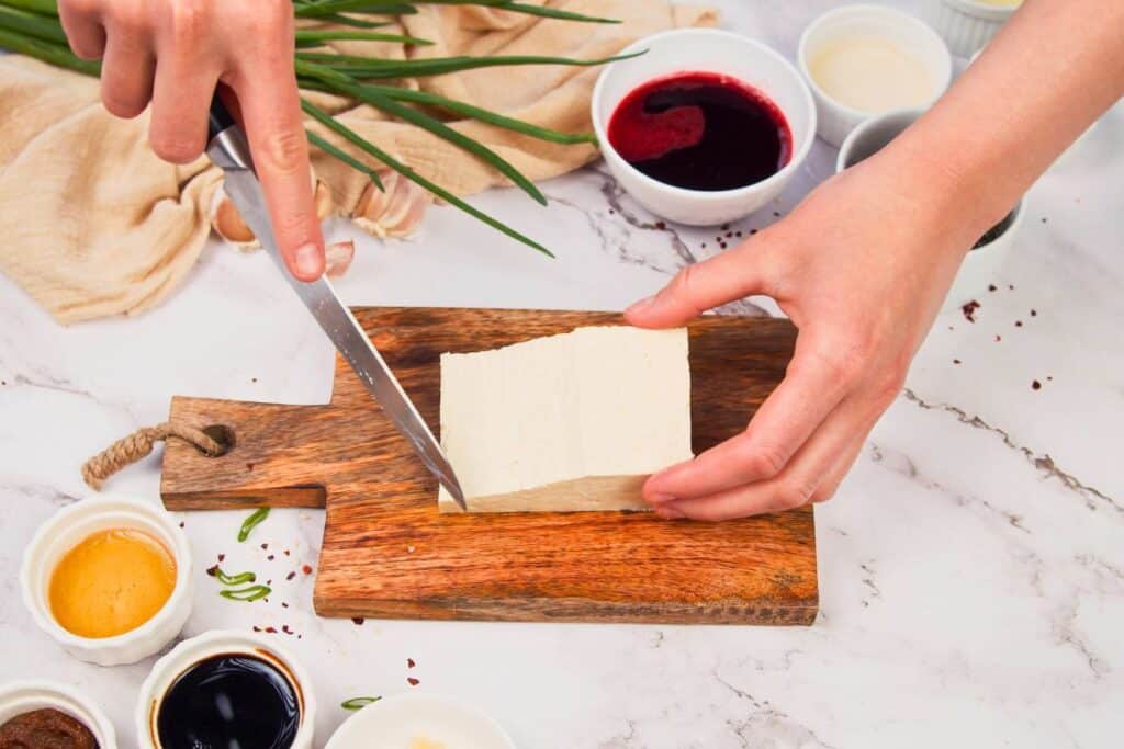 tofu on cutting board being sliced with knife