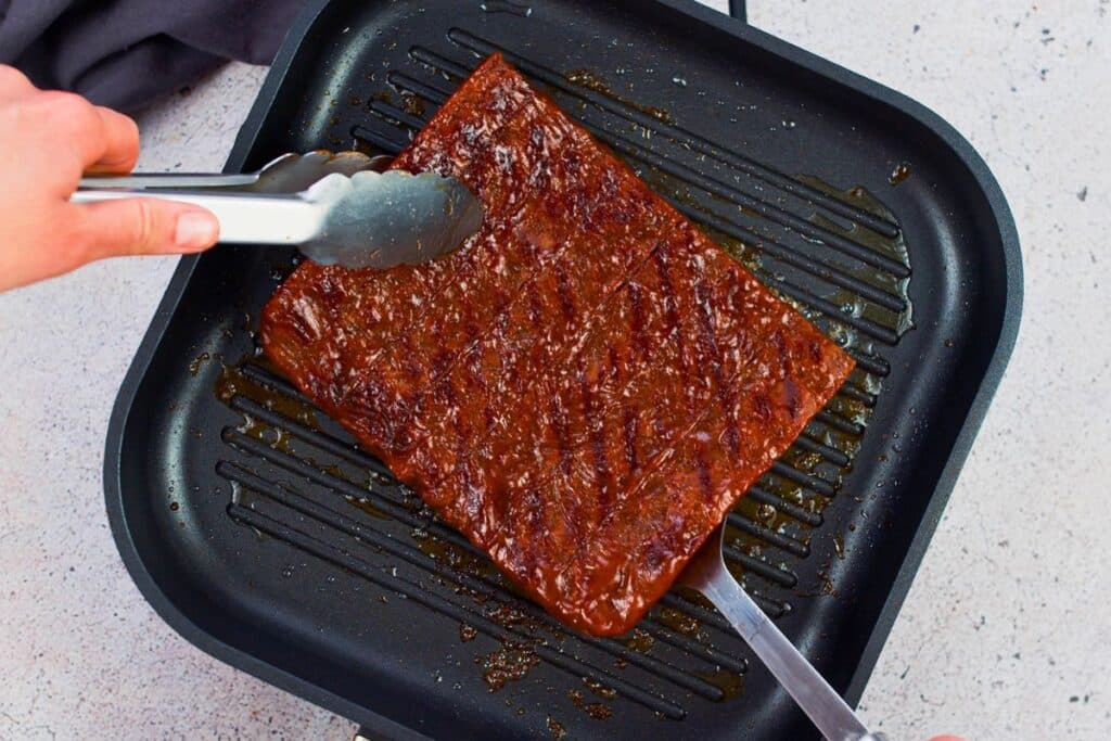 tongs picking vegan bbq ribs off grill pan