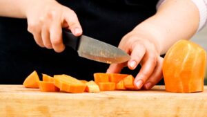 hand holding knife above sweet potato on cutting board