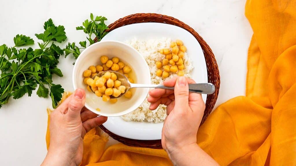 chickpeas being spooned over rice in white bowl