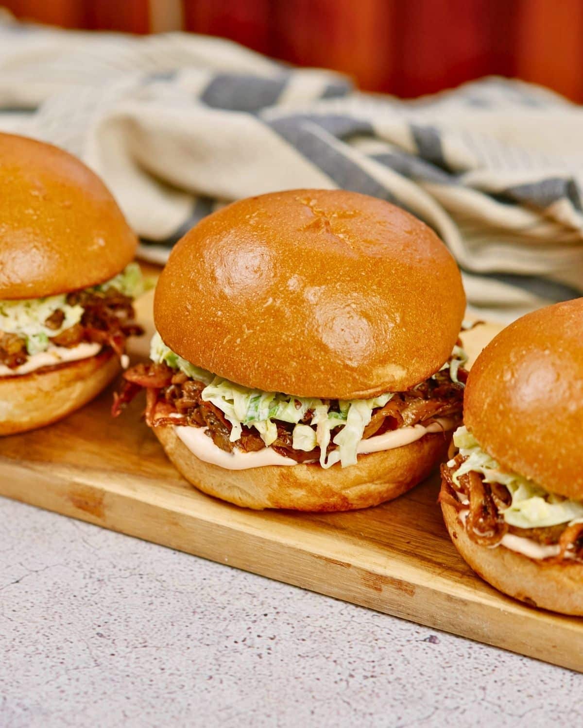 three vegan pulled pork sandwiches on wood platter