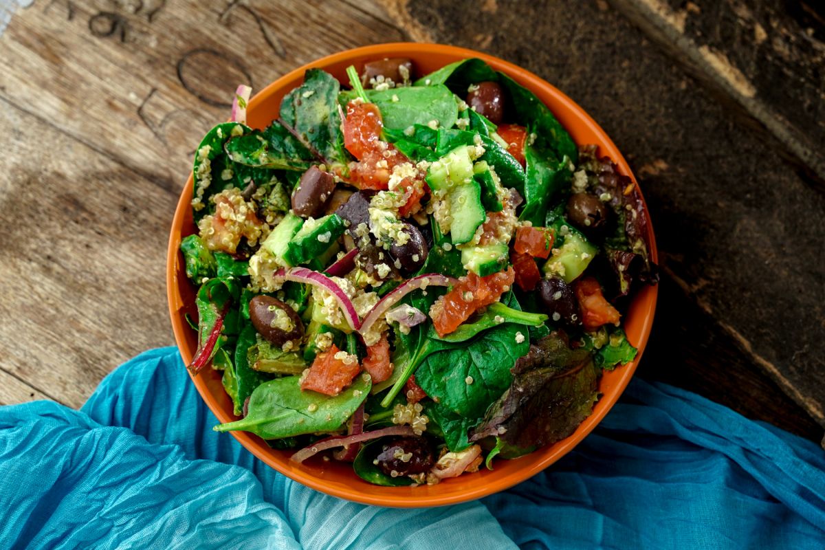 blue cloth napkin by orange bowl of spinach quinoa salad