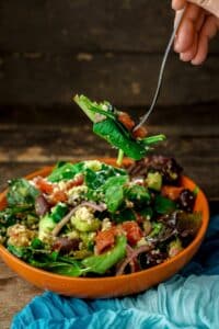 fork of spinach quinoa salad held above orange bowl