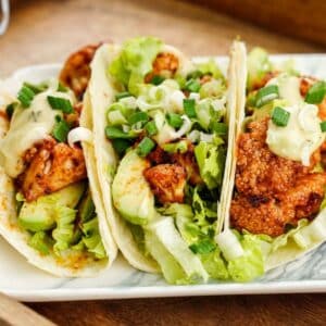 three tacos on plate topped with green onions and lettuce