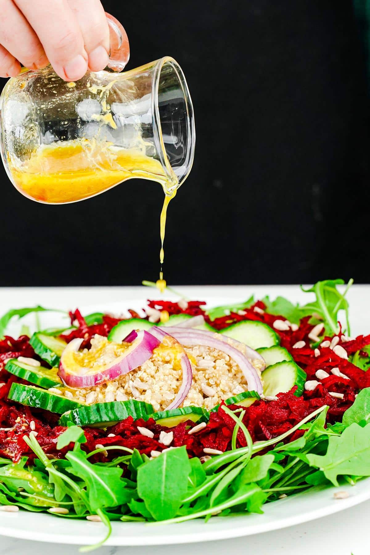 dressing being poured over the top of arugula salad