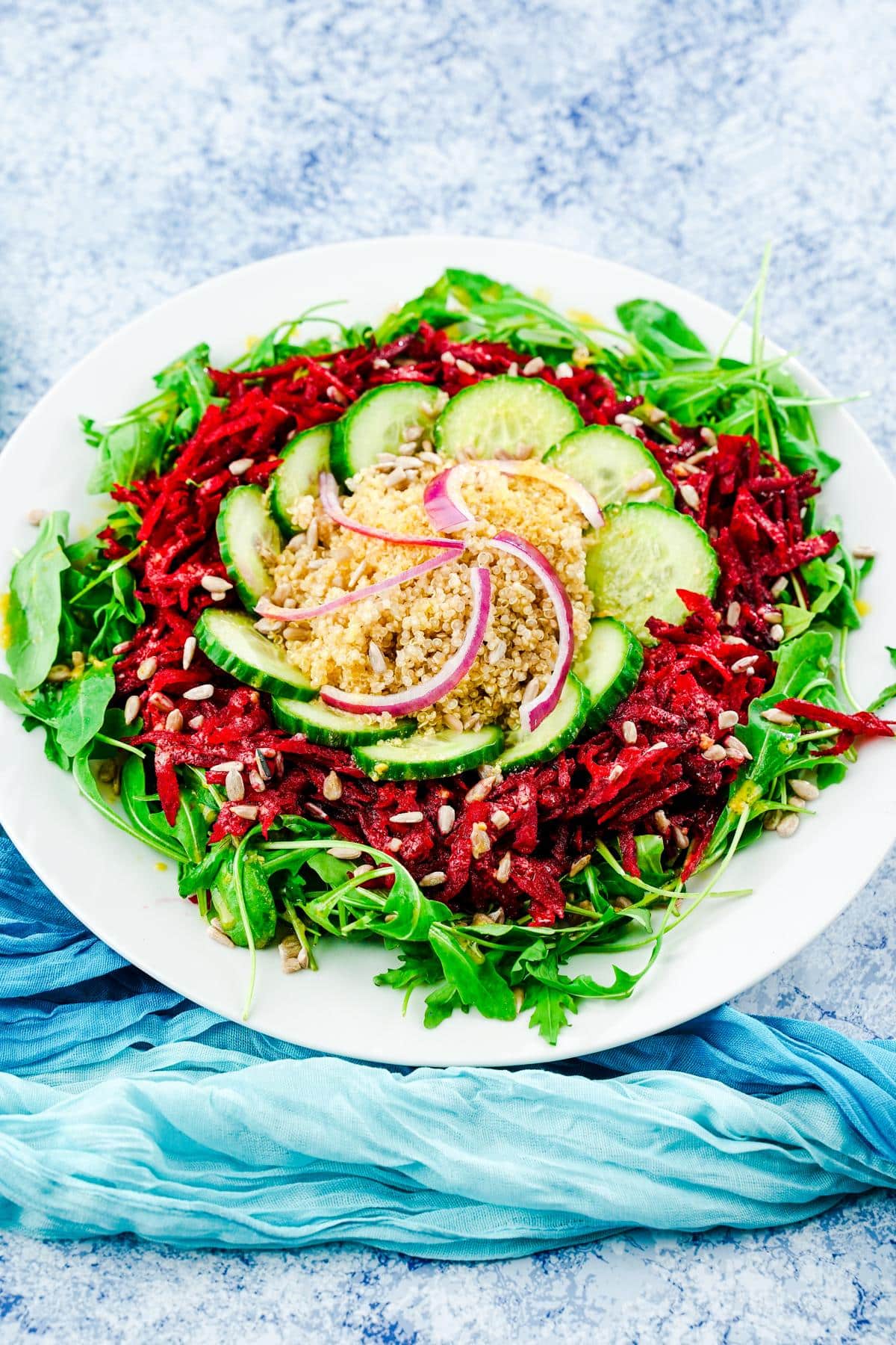 white plate of arugula salad topped by quinoa and beets on blue table