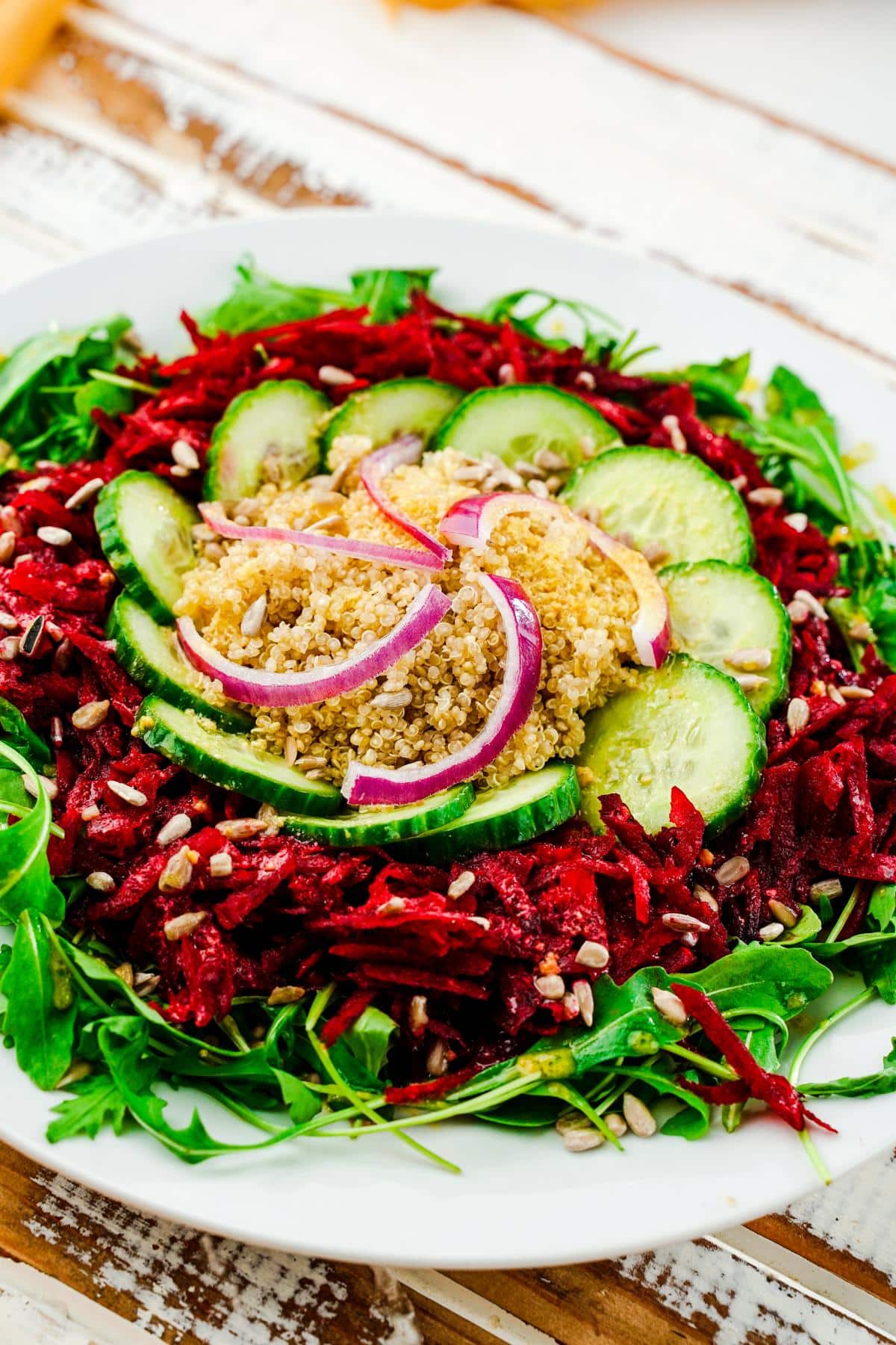 white plate of arugula salad topped with grated beets and cucumbers