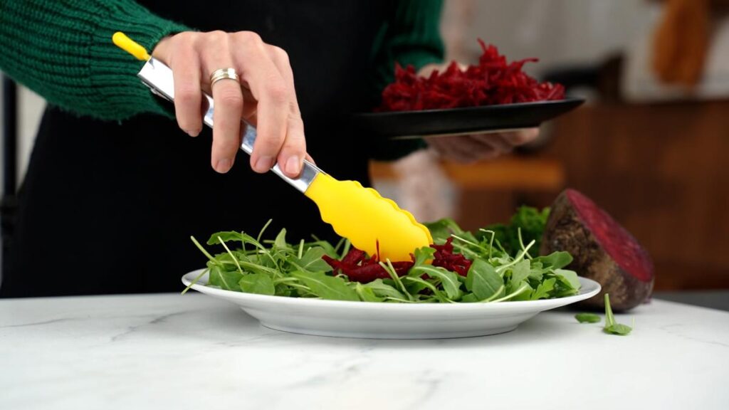 grated beets being placed on top of arugula salad